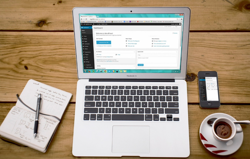 Building an Ecommerce Website with WordPress 1 MacBook showing WordPress dashboard with notebook, phone, and coffee on wooden desk